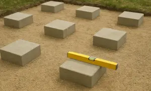 Betonowe bloczki ułożone na piasku, z poziomicą na jednym z nich.