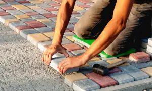 Ręczne układanie kostki brukowej na podłożu z betonu. Kolorowe kostki tworzą wzór.