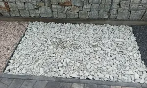 Jasny, biały kamień tworzy estetyczny podjazd z kamienia, kontrastując z gabionową ścianą i ciemniejszymi płytkami.