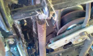 Mechanizm kosiarki traktorka MTD z widocznym pasem, sprężyną i kołami pasowymi. Pomoc w zrozumieniu, jak założyć pasek do kosiarki traktorka MTD.