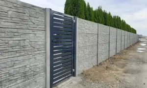 Betonowy płot z kamiennym wzorem i ciemnoszarą bramą.