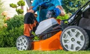 Mężczyzna wymienia baterię w pomarańczowej kosiarce akumulatorowej, przygotowując się do pracy w ogrodzie. To ważny element w rankingu kosiarek akumulatorowych.
