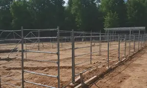 Budowa ogrodzenia z siatki i metalowych słupków na piaszczystym terenie, w tle drzewa.