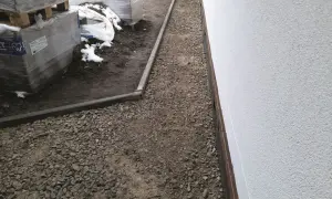 Nawierzchnia mineralna wokół budynku, obok palet z materiałami budowlanymi.
