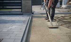 Pracownik równa podsypkę pod kostkę, przygotowując teren pod nową nawierzchnię.