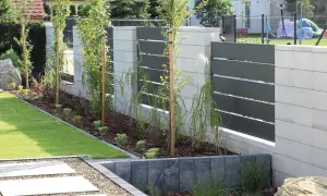 Nowoczesne ogrodzenie murowane z elementami metalowymi i zielenią.