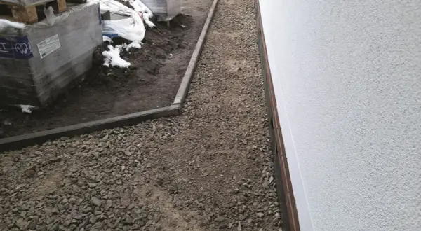 Nawierzchnia mineralna wokół budynku, obok palet z materiałami budowlanymi.