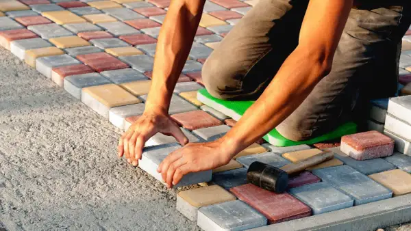 Ręczne układanie kostki brukowej na podłożu z betonu. Kolorowe kostki tworzą wzór.