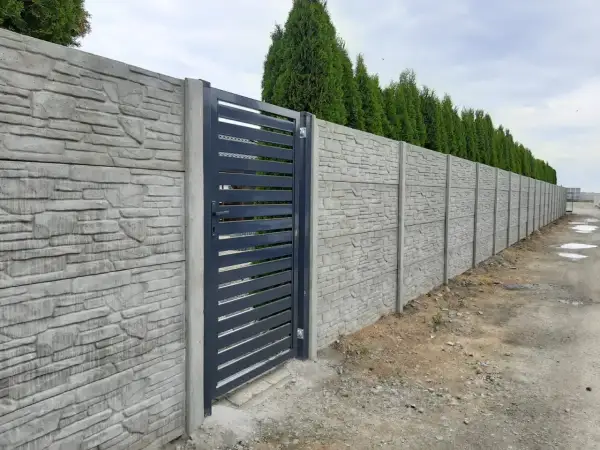 Betonowy płot z kamiennym wzorem i ciemnoszarą bramą.