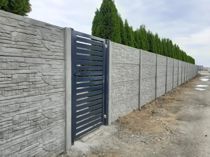 Betonowy płot z kamiennym wzorem i ciemnoszarą bramą.